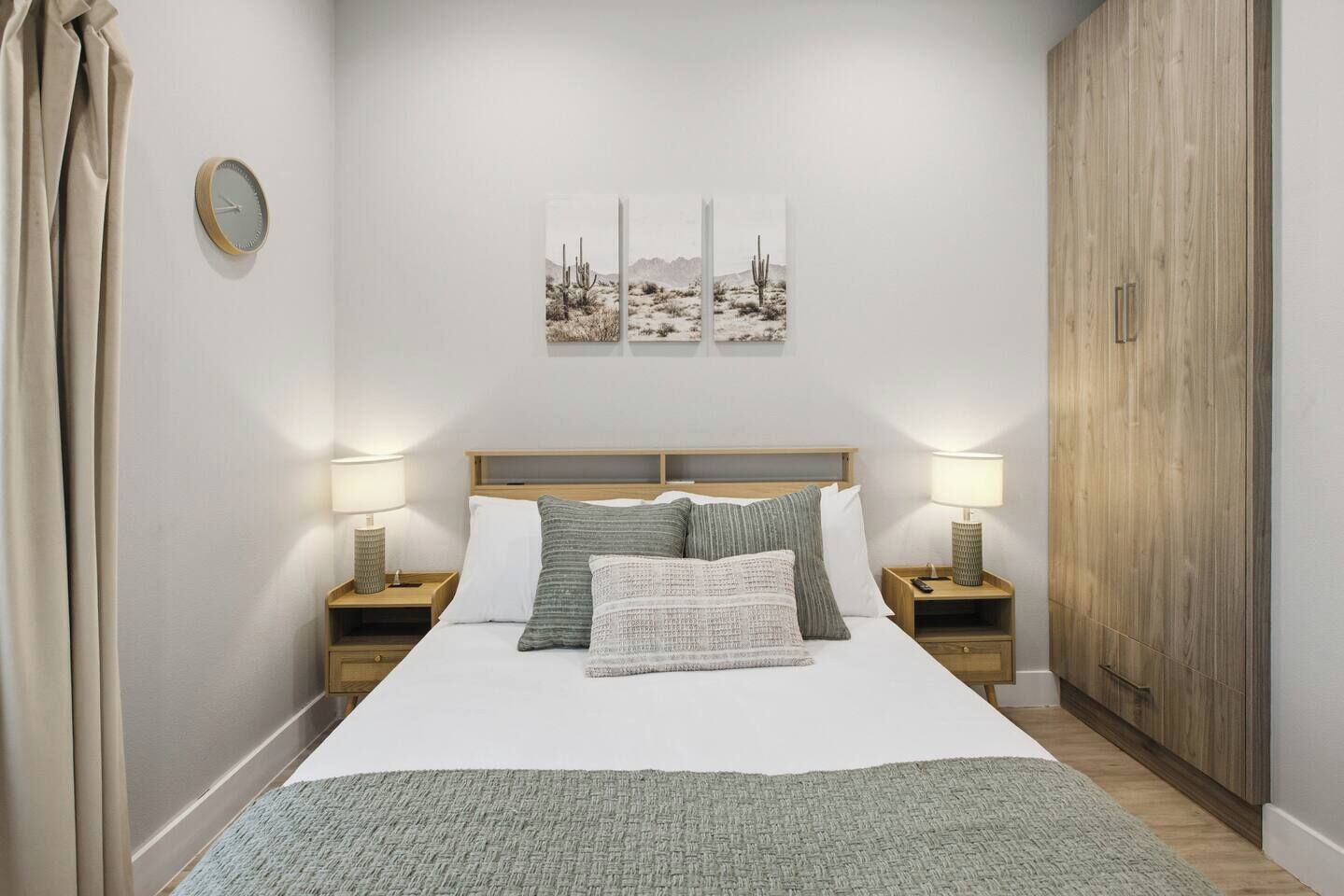 A bedroom with a bed, two bedside tables, a clock, a painting, and a wardrobe.