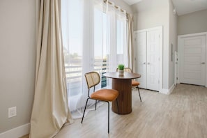 Quarto com uma mesa de jantar, duas cadeiras, um vaso de planta e vista através de amplas janelas.