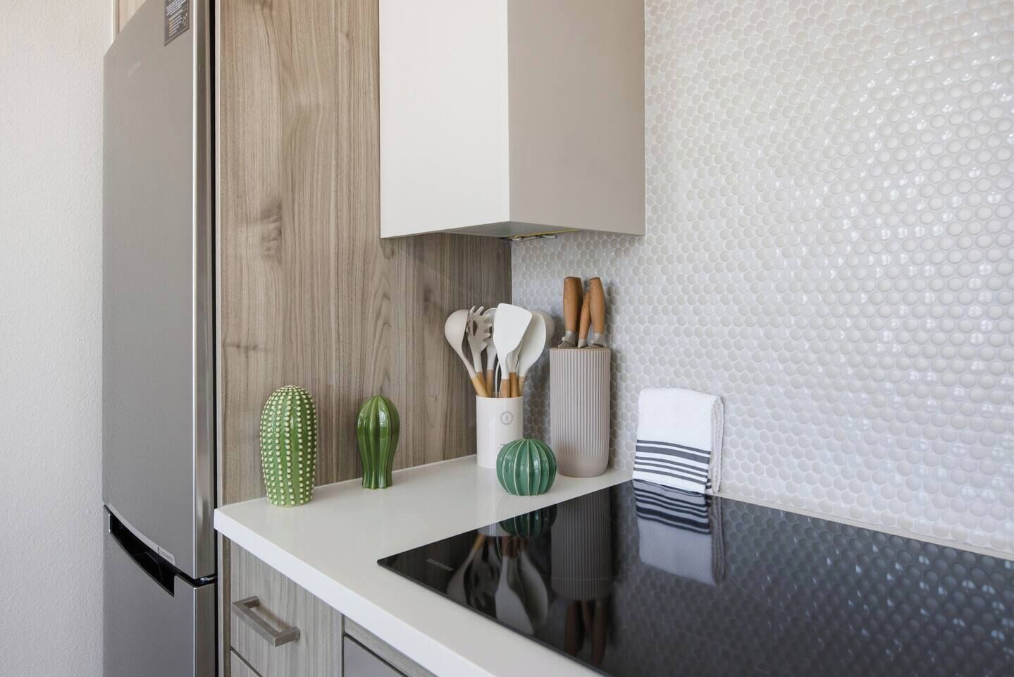 A kitchen counter with a white cabinet, a cactus, a green vase, a white container with utensils, and a striped towel.