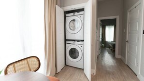 A laundry room with two stacked washing machines, a dining area with a table and chair, and a hallway leading to another room. - Stockyards + Downtown | Bright 1BR | Sleeps 3 - Apartment (Fort Worth)