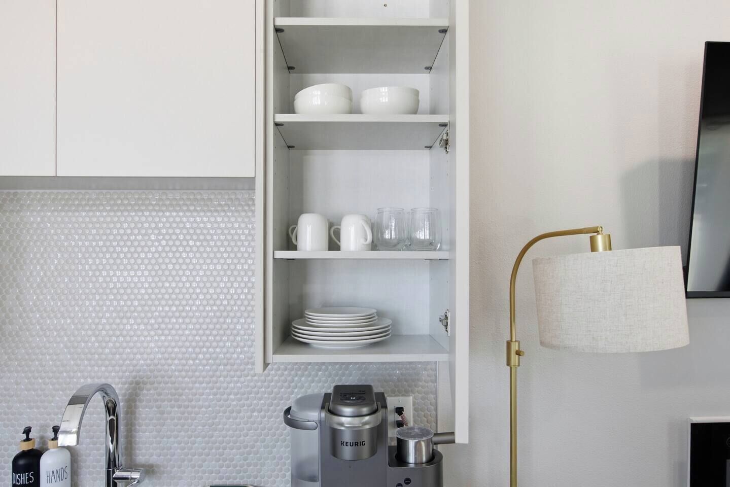 A kitchen with white cabinets, a coffee maker, and a wall-mounted lamp.