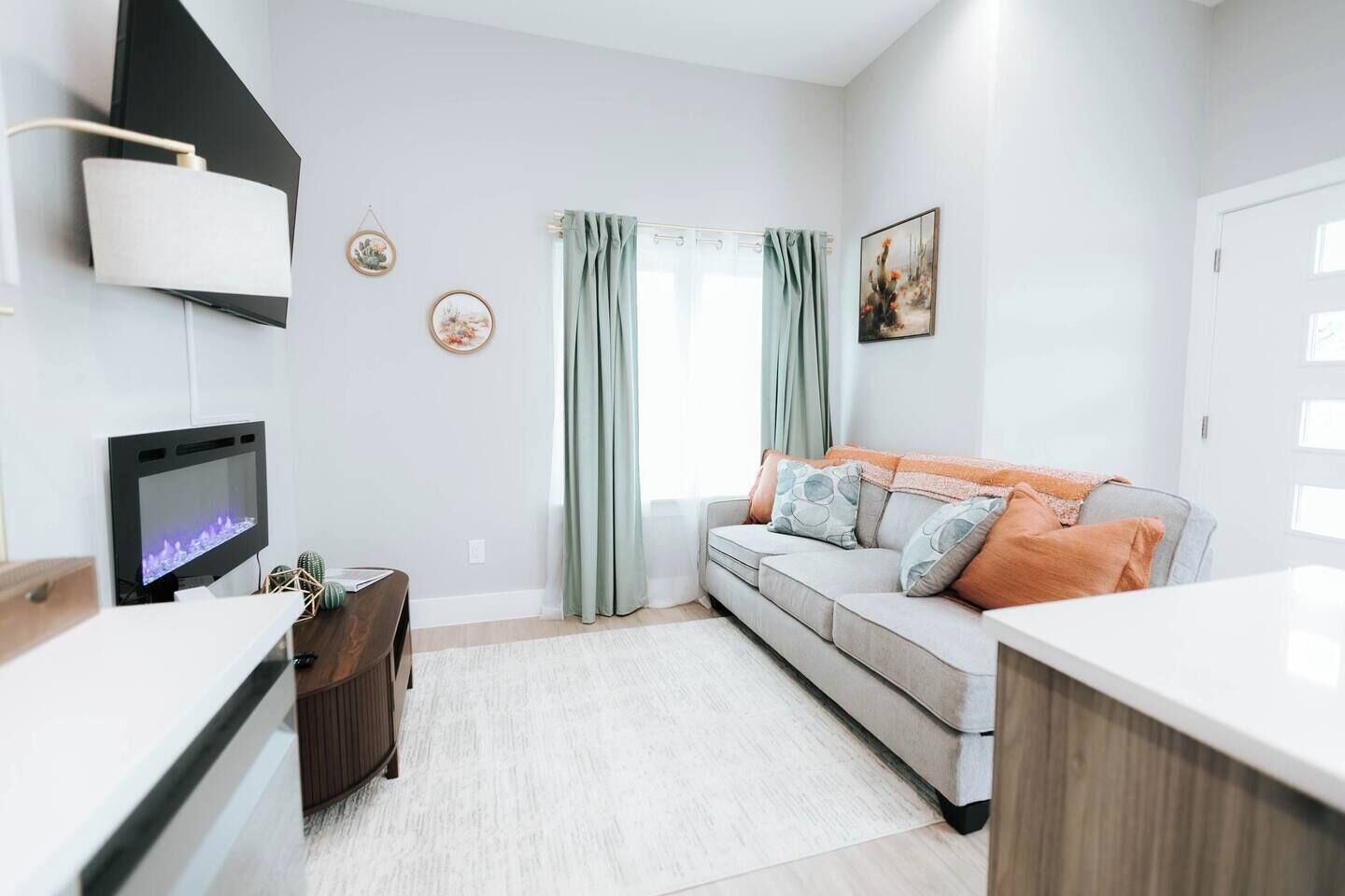 Ein modernes Wohnzimmer mit Flachbildfernseher, einer Couch mit Kissen, einem Couchtisch und einem Essbereich mit einem Stuhl.