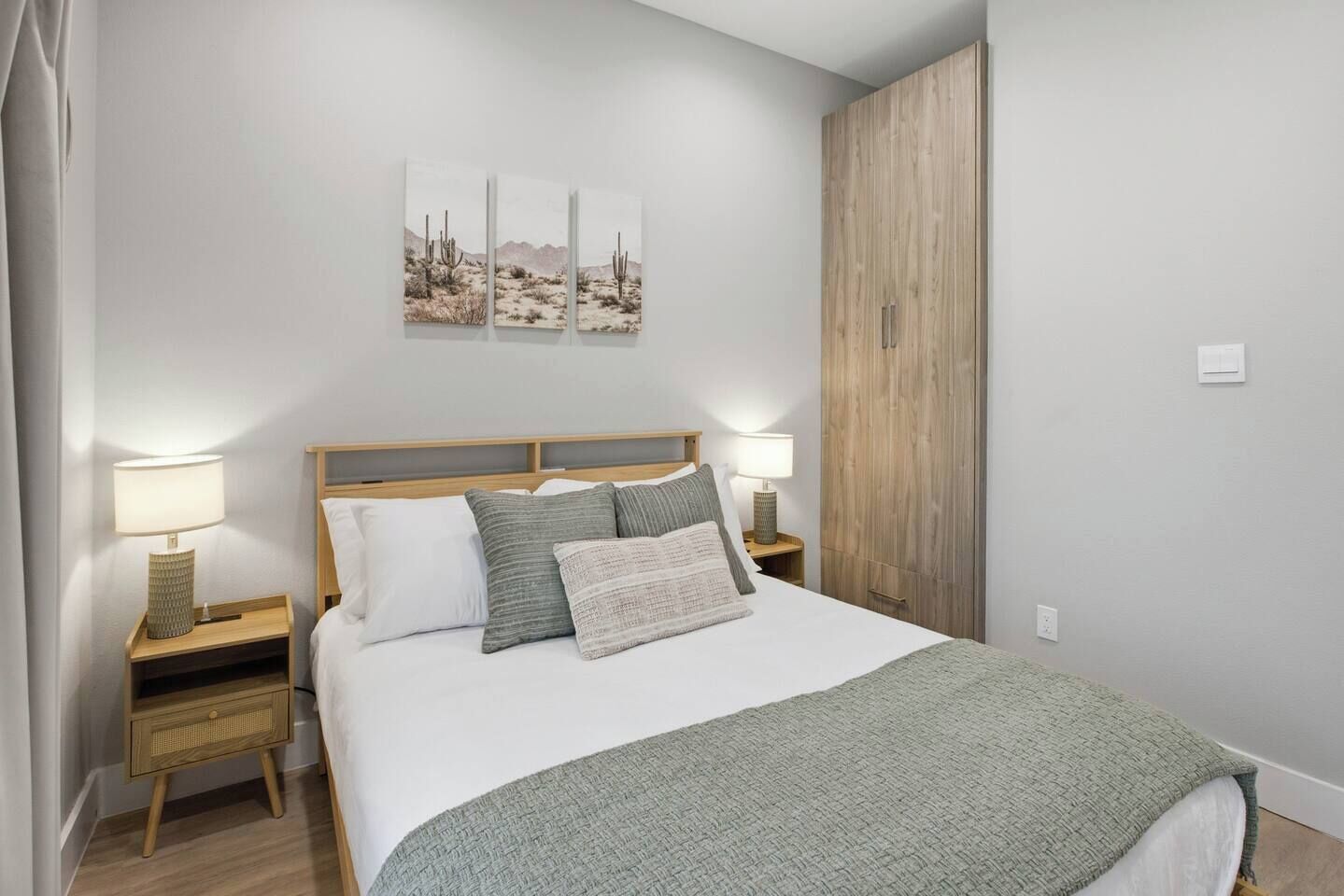 Een slaapkamer met een bed, twee nachtkastjes, een houten garderobe en wanddecoratie met een woestijnmotief.