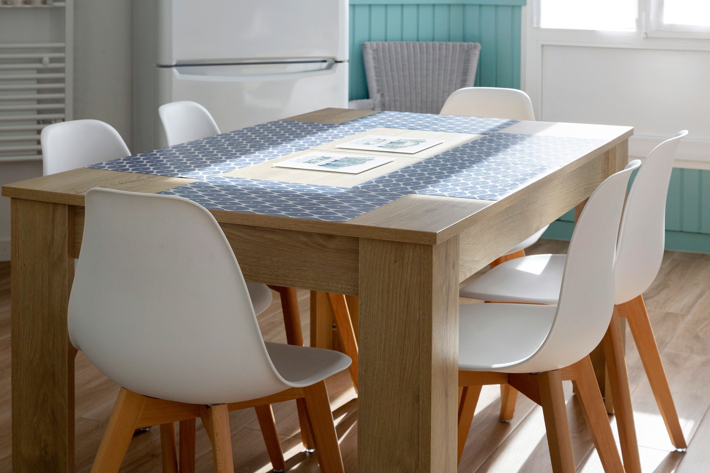 A dining table with a patterned tablecloth, surrounded by white chairs with wooden legs.