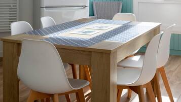 A dining table with a patterned tablecloth, surrounded by white chairs with wooden legs.
