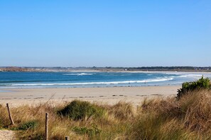 Une plage avec des vagues, un ciel dégagé et des bâtiments qui se dessinent à l’horizon.