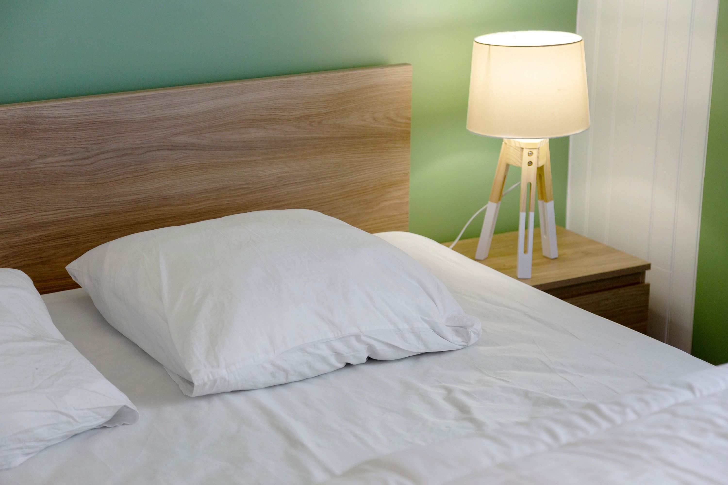 Una cama con ropa de cama y almohadas blancas, un cabecero de madera y una mesita de noche con lámpara.