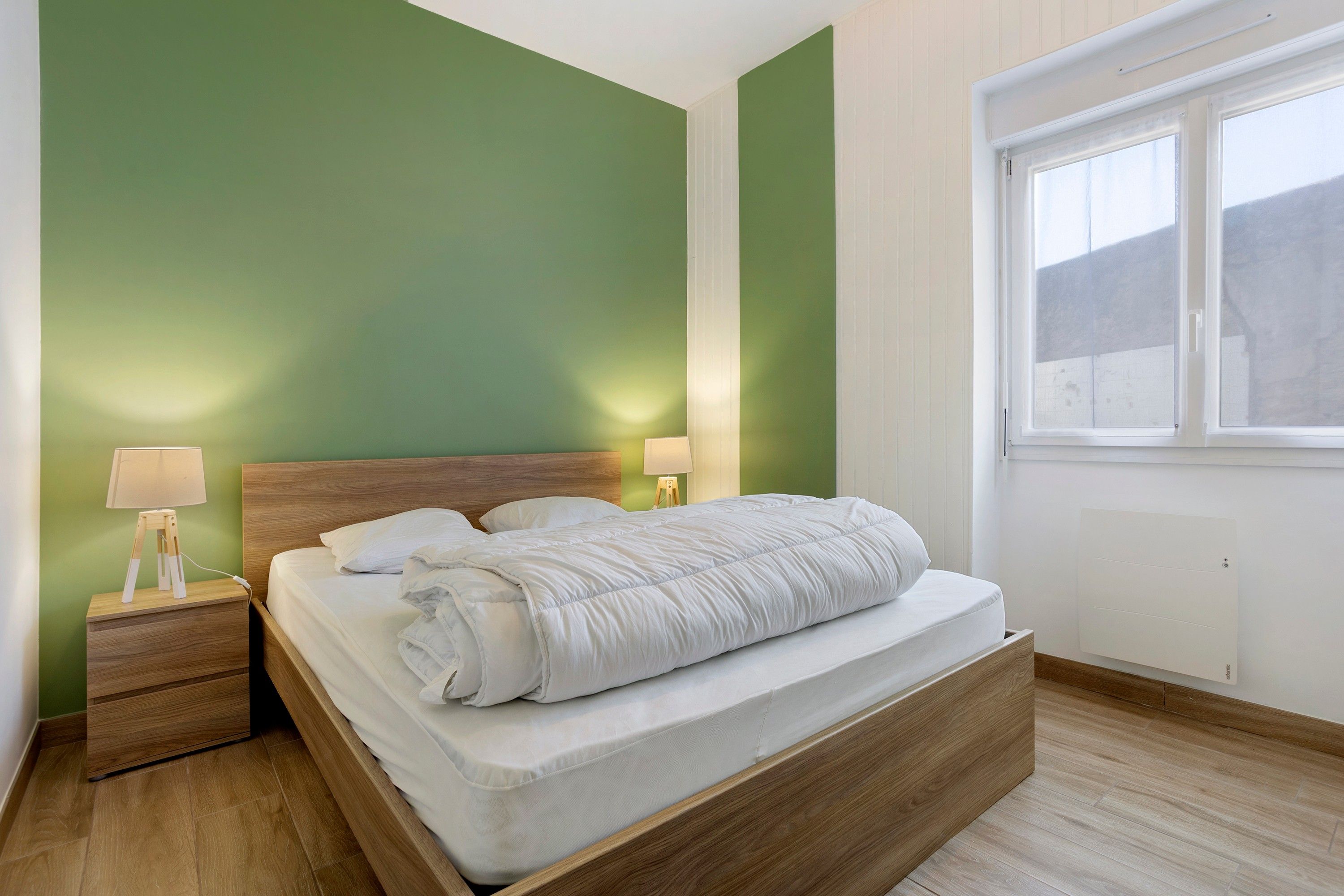 Ein Schlafzimmer mit einem Bett, Nachttischlampen, einem Fenster und einer grünen Wand.
