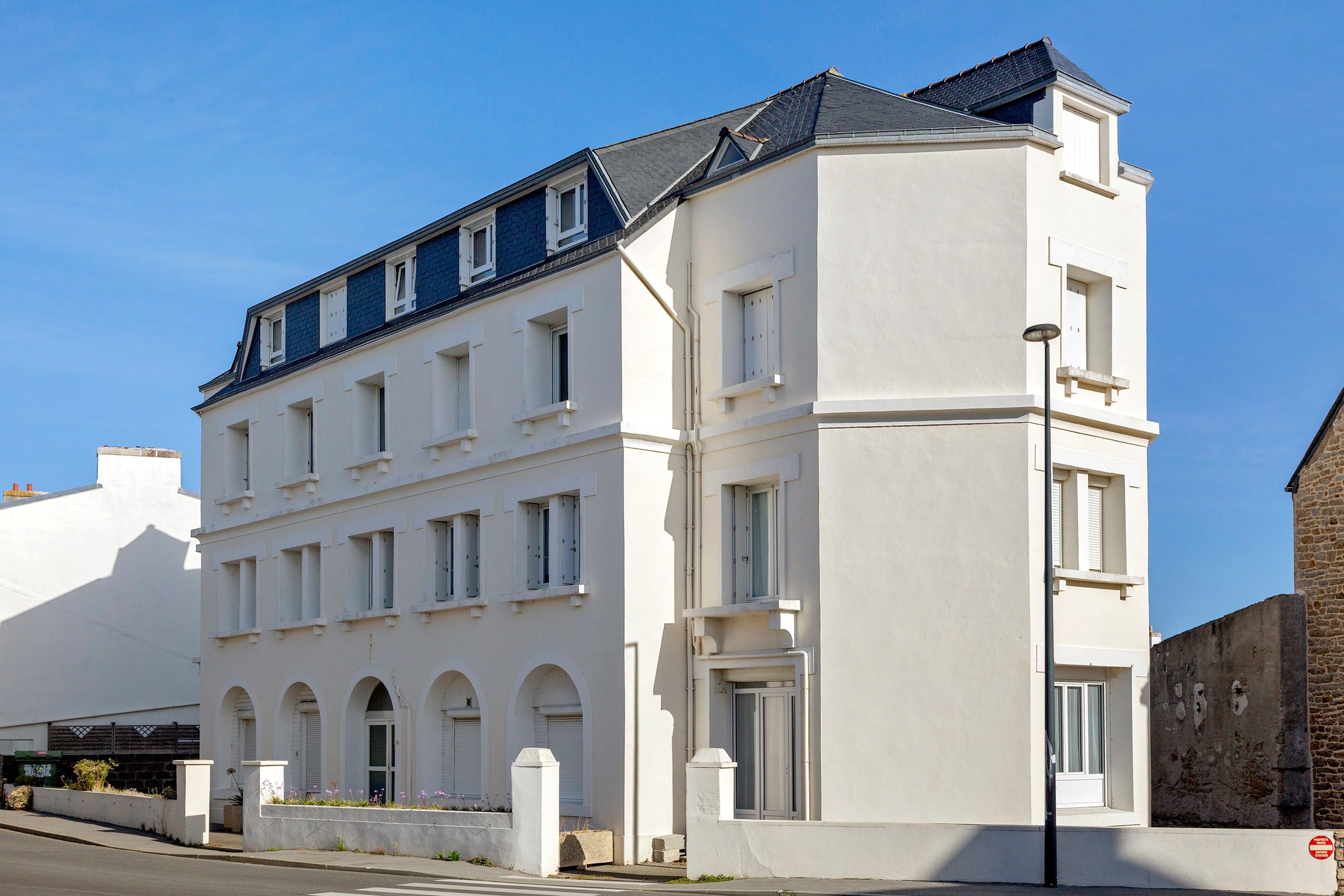 Ein mehrstöckiges Gebäude mit flachem Dach, zahlreichen Fenstern und einer weißen Fassade.