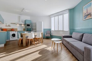 A modern kitchen with a dining area, a sofa, and a window with blinds. - Bright Apartment Near the Sea with Wi-Fi (Penmarch)