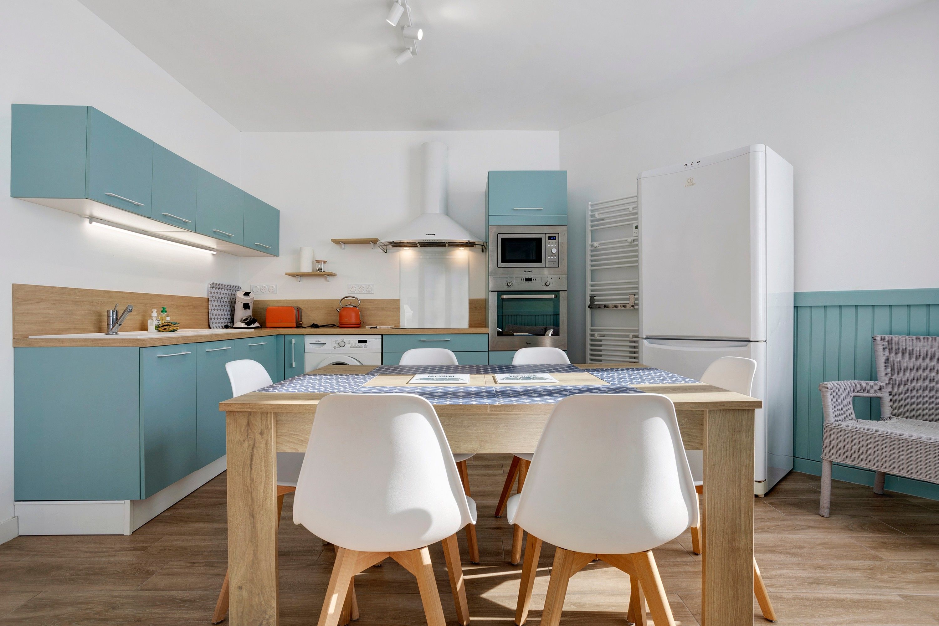 Een moderne keuken met blauwgroene kastjes, een houten tafel en witte stoelen.