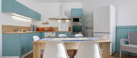 A modern kitchen with teal cabinets, a wooden table, and white chairs.