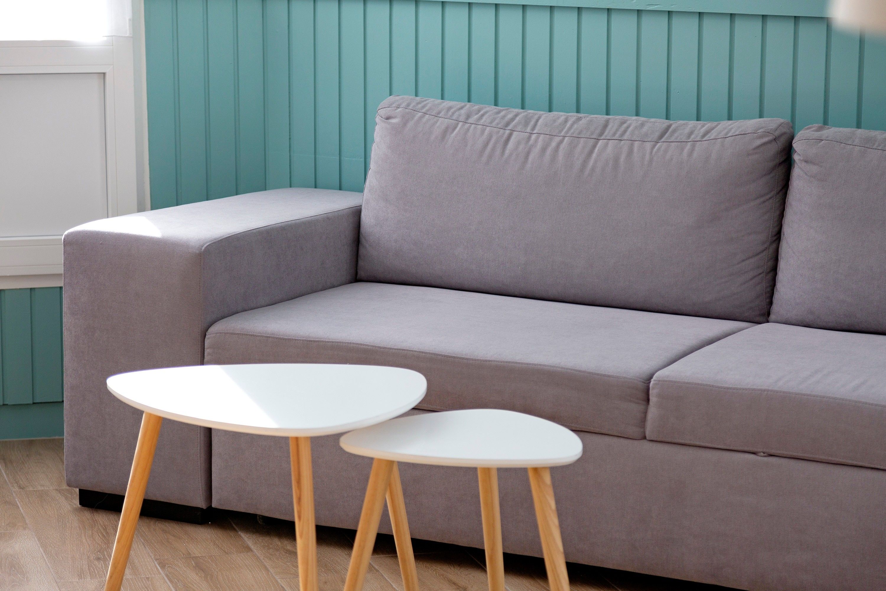 Un canapé gris, une table blanche et des pieds en bois, le tout dans une pièce aux murs de couleur turquoise.