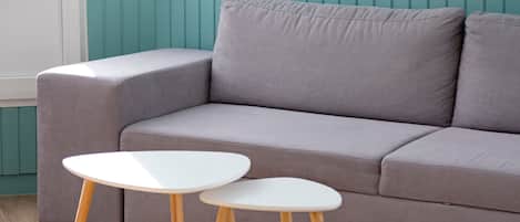 A grey sofa with a white table and wooden legs in a room with teal walls.
