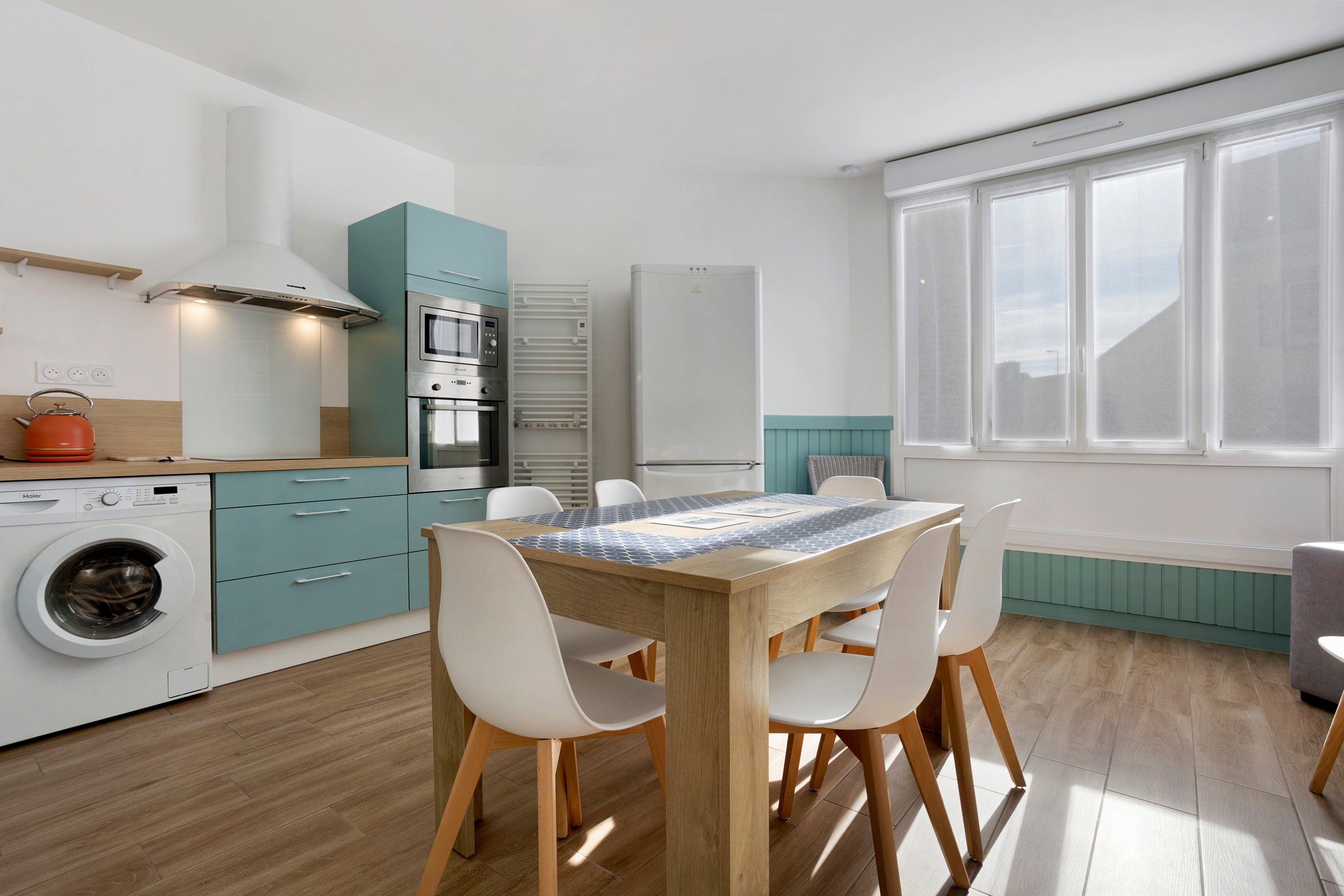 A modern kitchen with a dining area, including a washing machine, oven, and a window with a view.
