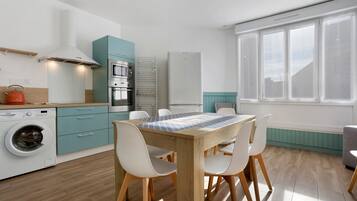 A modern kitchen with a dining area, including a washing machine, oven, and a window with a view.