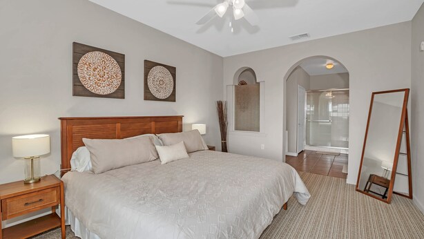A bedroom with a bed, nightstand, wall art, ceiling fan, and a mirror. - Upstay Large Family Condo w Pool, Sauna (Winter Garden)