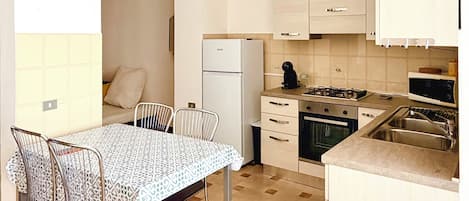 Uma cozinha compacta com geladeira, fogão, micro-ondas e pia.