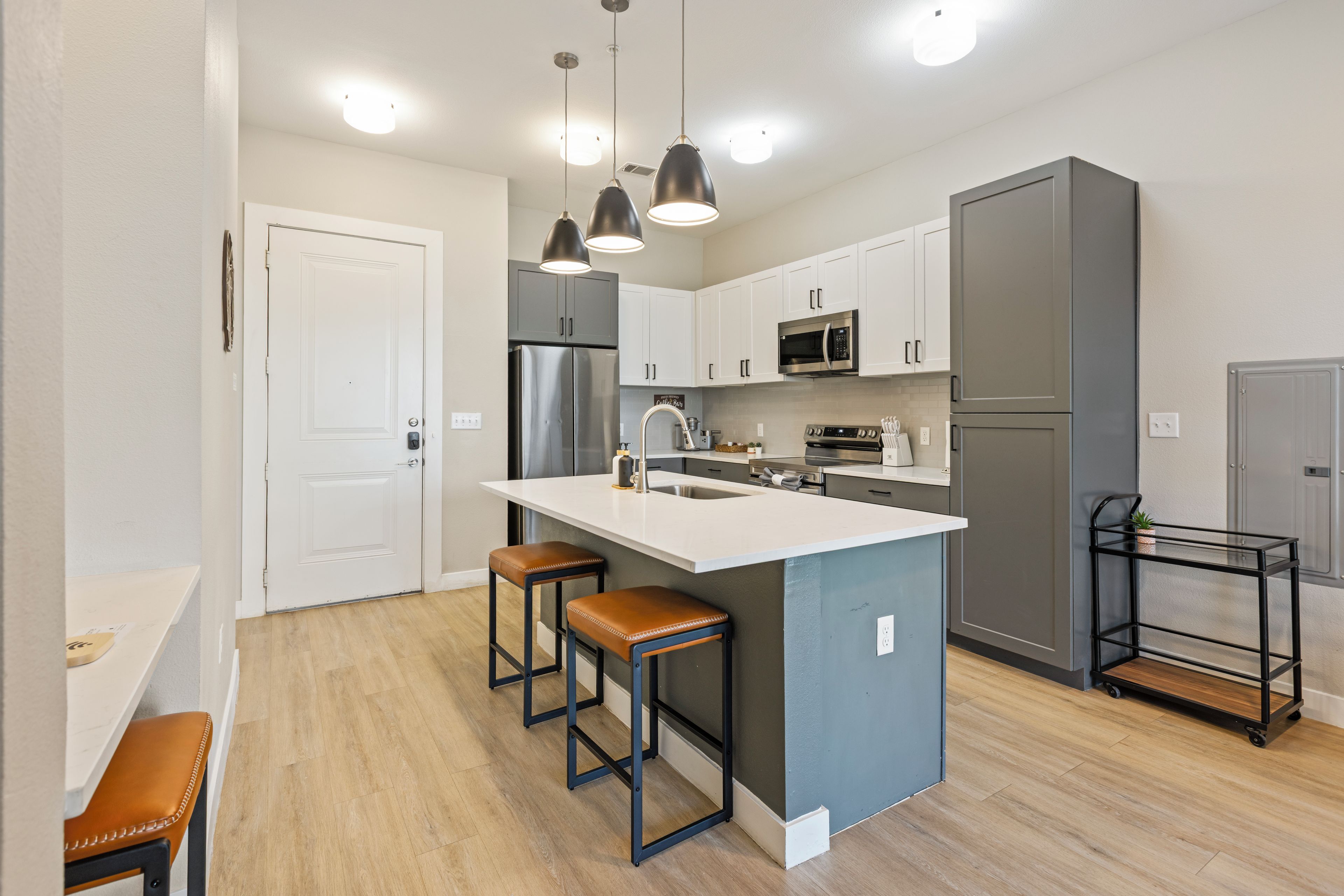 A modern kitchen with a central island, bar stools, stainless steel appliances, and pendant lighting.