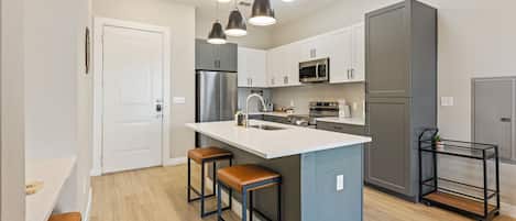 A modern kitchen with a central island, bar stools, stainless steel appliances, and pendant lighting.