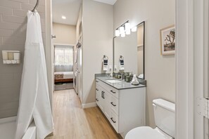 A modern bathroom with a shower, toilet, sink, and a large mirror. - Balcony Near Downtown & Med Center | Sleeps 4 (Fort Worth)