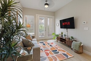 A living room with a sofa, a coffee table, a TV, and a plant. - Balcony Near Downtown & Med Center | Sleeps 4 (Fort Worth)