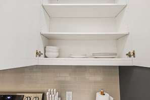 Een keuken met witte kasten, een betegelde spatwand en een digitale klok die de tijd toont.