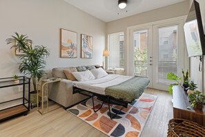 A modern bedroom with a bed, bedside tables, a desk, a chair, and a TV. - Balcony Near Downtown & Med Center | Sleeps 4 (Fort Worth)