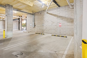 Een parkeergarage binnen met betonnen muren, een plafond met blootliggende leidingen en een bakstenen muur met een bord 'Gereserveerd parkeren'.