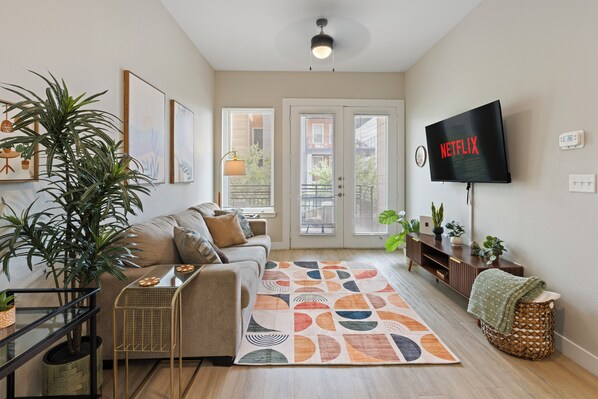 A living room with a sofa, a coffee table, a TV, and a large plant. - Balcony Near Downtown & Med Center | Sleeps 4 (Fort Worth)