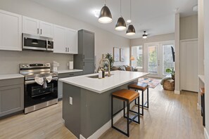 A modern kitchen with stainless steel appliances, a central island with stools, and pendant lighting. - Balcony Near Downtown & Med Center | Sleeps 4 (Fort Worth)