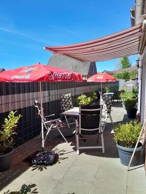 Ein Patio im Freien mit einer Sitzgruppe, Sonnenschirmen und Topfpflanzen.