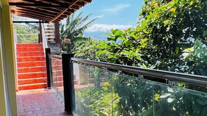 Un balcón techado con suelo de ladrillo, barandilla de vidrio y vistas a la vegetación.