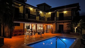 Una casa de dos pisos con piscina, mobiliario exterior y palmeras.