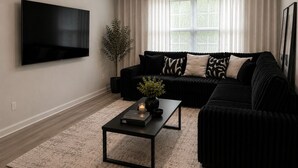 A living room with a black sofa, a flat-screen TV, a potted plant, and a coffee table.