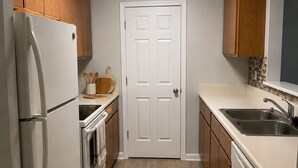 A kitchen with wooden cabinets, a white refrigerator, an oven, a sink, and a door.