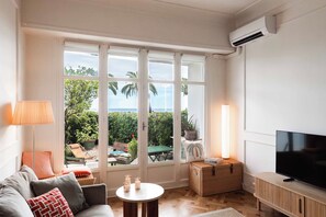 Ein Wohnzimmer mit einer Couch, einem Fernseher, einem Tisch mit Kerzen und Blick auf Grünfläche draußen.