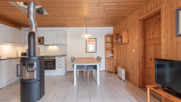 A modern kitchen with a wood stove, white cabinets, and a dining area with a table and chairs. - Gemutlicher Doppelbungalow mit Garten und Kaminofen in Mirow (Mirow)