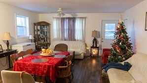 A cozy living room with a dining table, a Christmas tree, a sofa, and a ceiling fan. - Country in the City: Quiet, central home with golf views, near Victoria Park. (Truro)