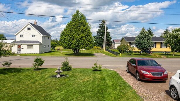 A residential street with houses, a red car, and a clear sky. - Country in the City: Quiet, central home with golf views, near Victoria Park. (Truro)