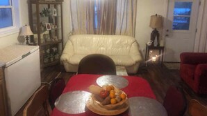 A living room with a dining table set for two, a sofa, a cabinet with decorative items, and a door with a view. - Country in the City: Quiet, central home with golf views, near Victoria Park. (Truro)