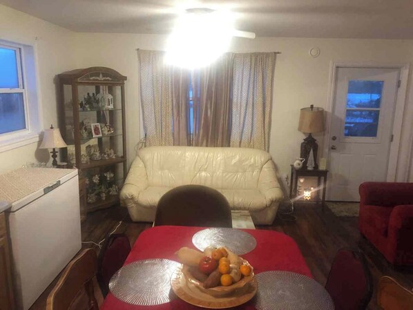 Una sala de estar con una mesa de comedor lista para dos personas, un sofá, un aparador con adornos y una puerta con vistas.