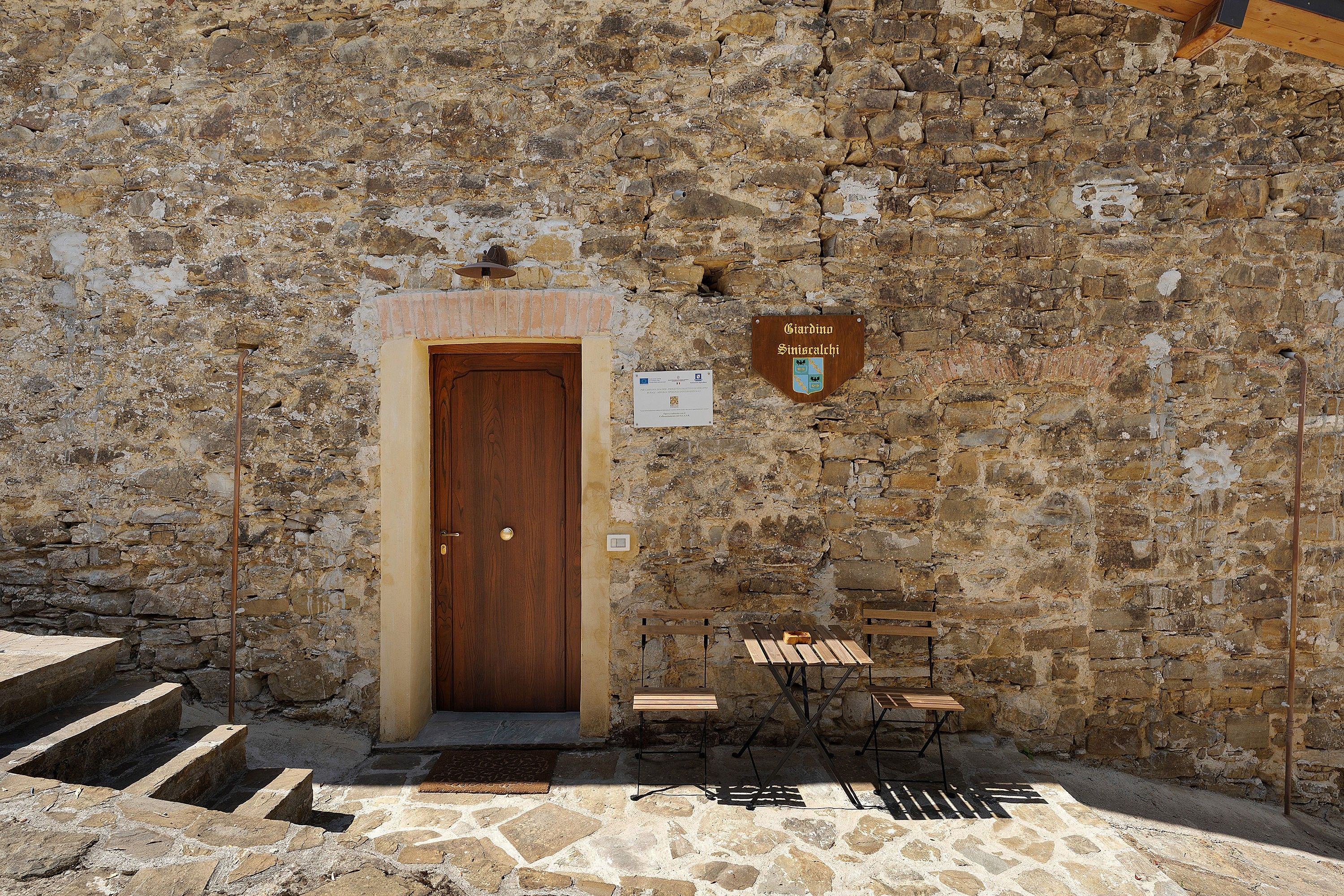 A stone building with a wooden door, a bench, and a table outside.