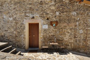 A stone building with a wooden door, a bench, and a table outside.
