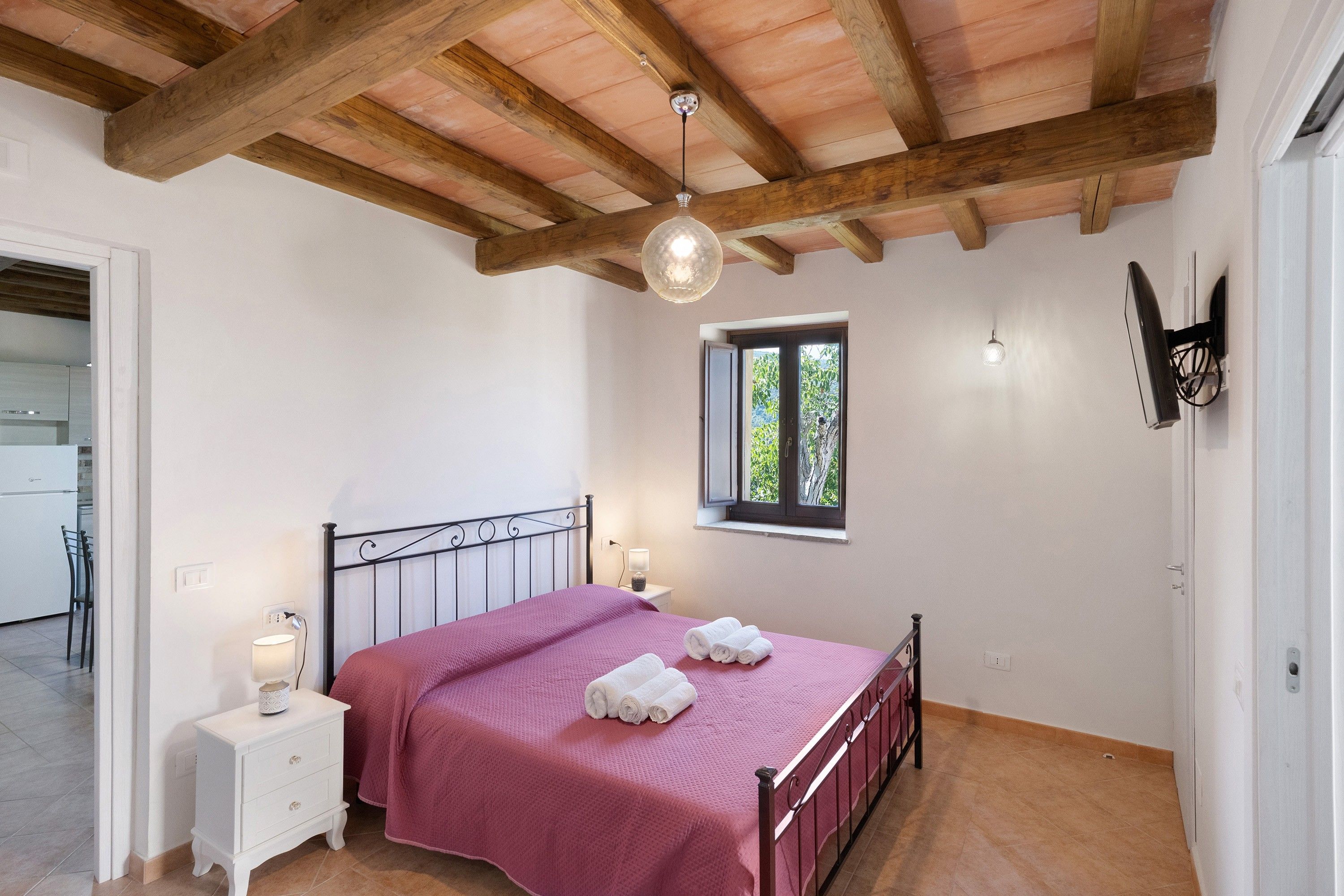 Une chambre à coucher avec un lit, des tables de chevet, une fenêtre et un ventilateur de plafond.