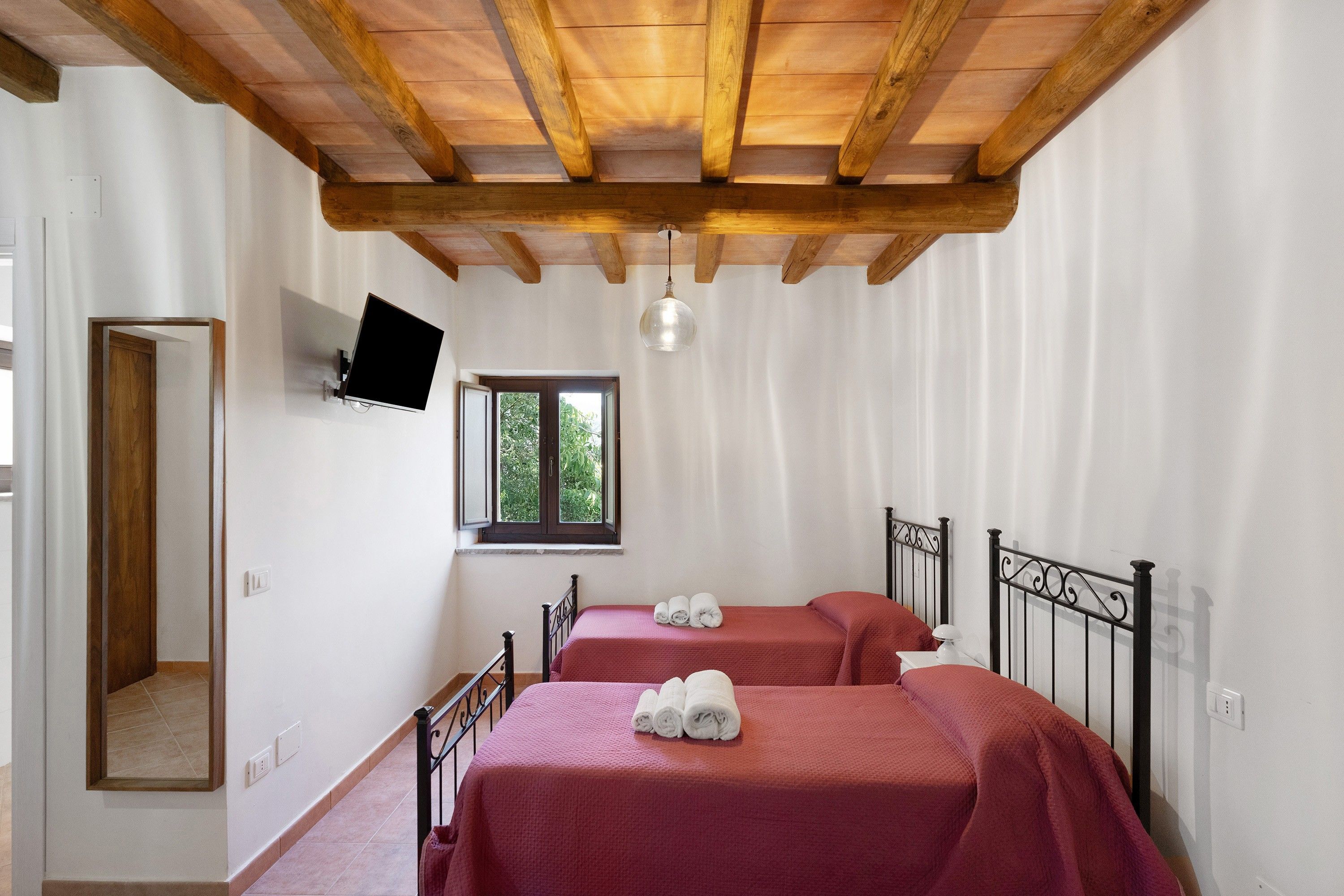 Une chambre avec deux lits, un téléviseur fixé au mur, une fenêtre donnant sur un paysage verdoyant et un plafond en bois.