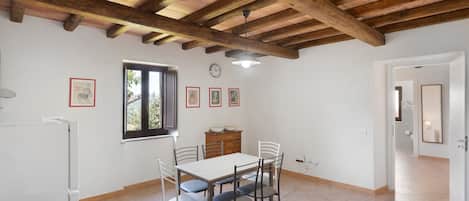 A dining area with a wooden ceiling, a dining table with chairs, a window, and a clock on the wall.