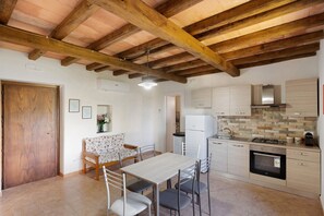 A compact kitchen with a dining area, wooden ceiling beams, and a tiled floor. - Giardino Siniscalchi – Apartment 1 with Wi-Fi and Air Conditioning (Copersito)
