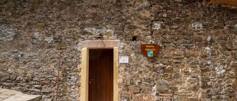 Un edificio de piedra con puerta de madera, una placa y asientos al aire libre.