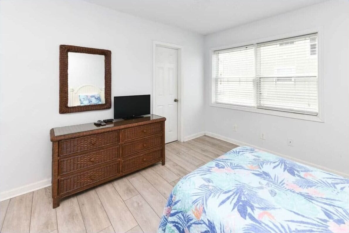 A bedroom with a bed, dresser, mirror, and window.